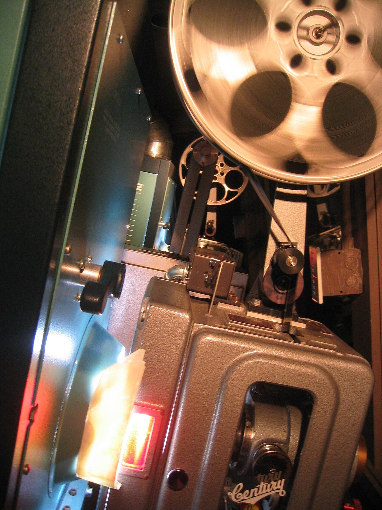 Close-up of an old film projector with a large metal reel on top and a glowing orange light near the lens