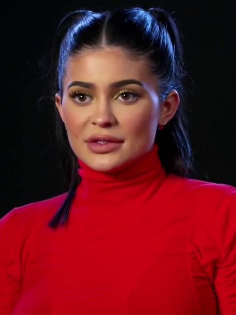 Kylie Jenner, with dark hair pulled back, wears a red turtleneck against a dark background