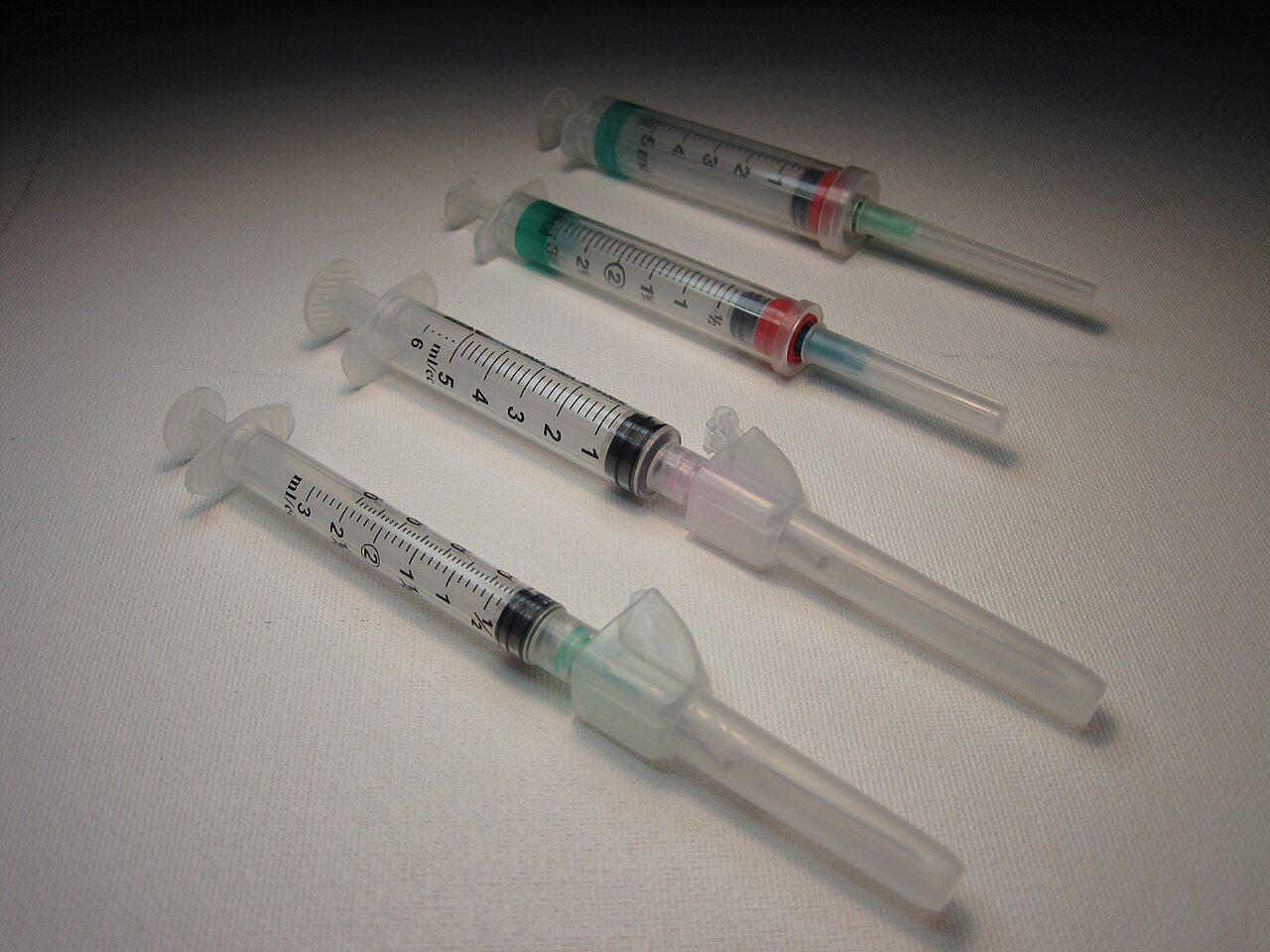 Three plastic syringes with needles and caps lying on a white surface