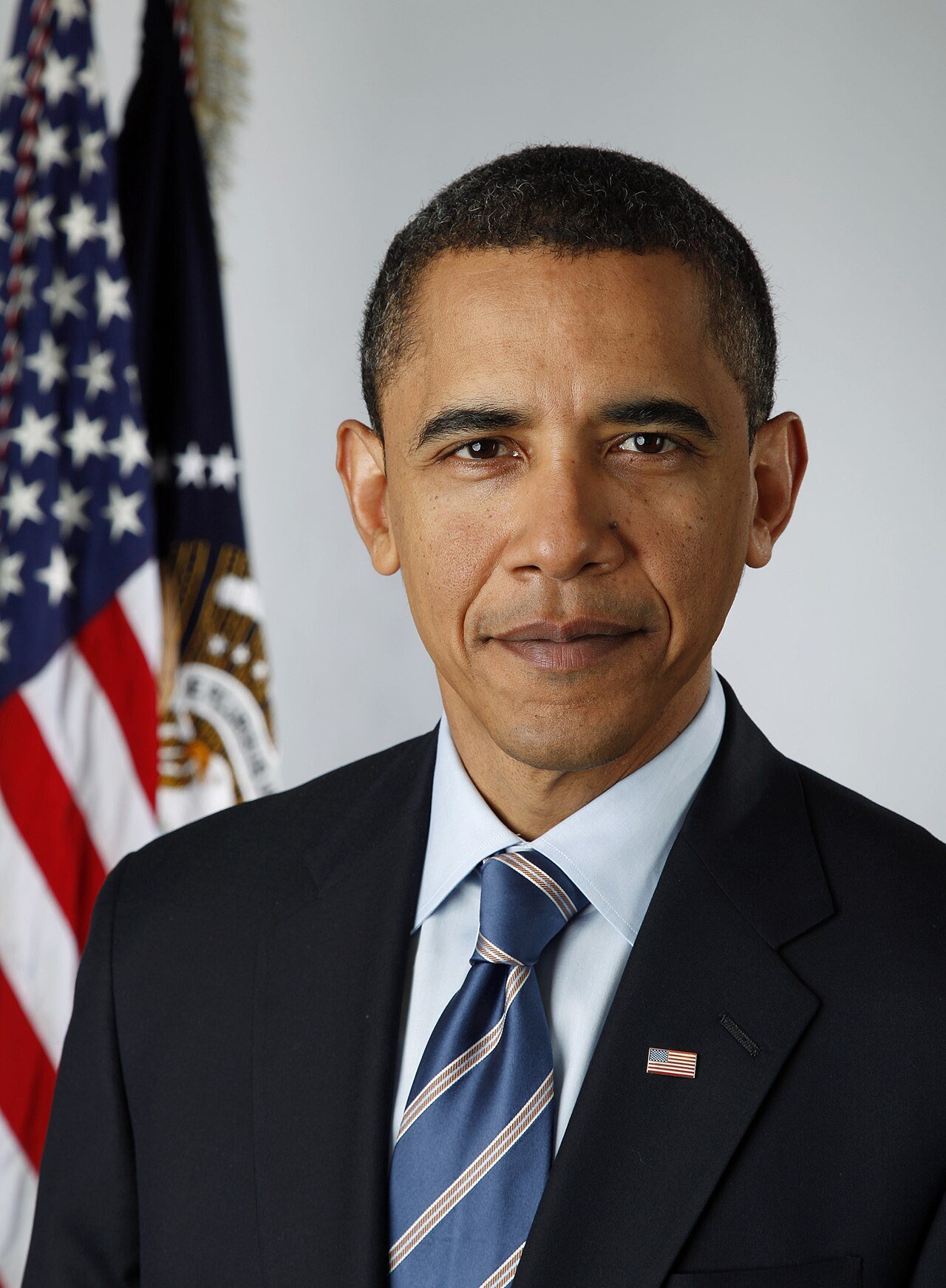 Official portrait of a man in a dark suit and blue striped tie standing in front of an American flag