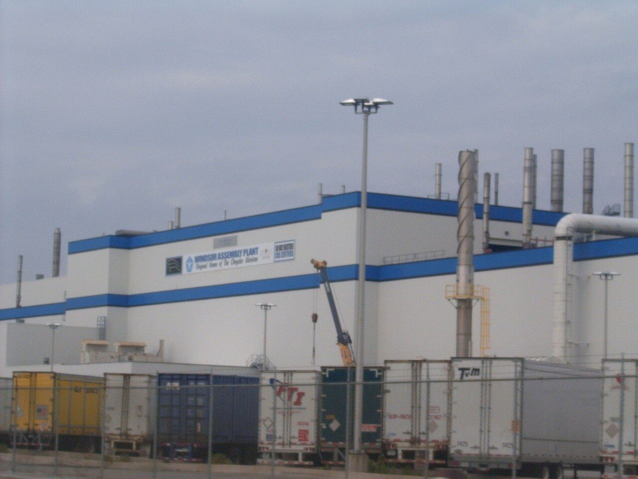 Exterior of a large auto assembly plant building with parking and trees in the foreground