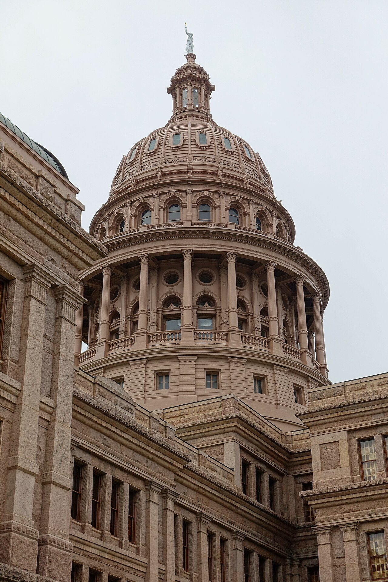 The tall pink granite dome of the Texas State Capitol rises above the building against a pale sky
