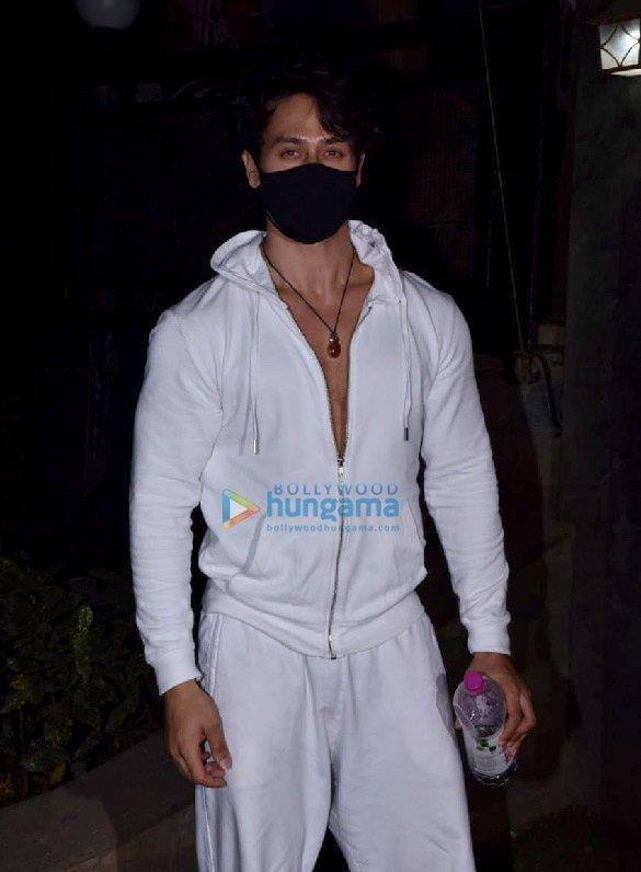 Actor Tiger Shroff in a white hooded tracksuit and a black face mask stands outside at night holding a water bottle