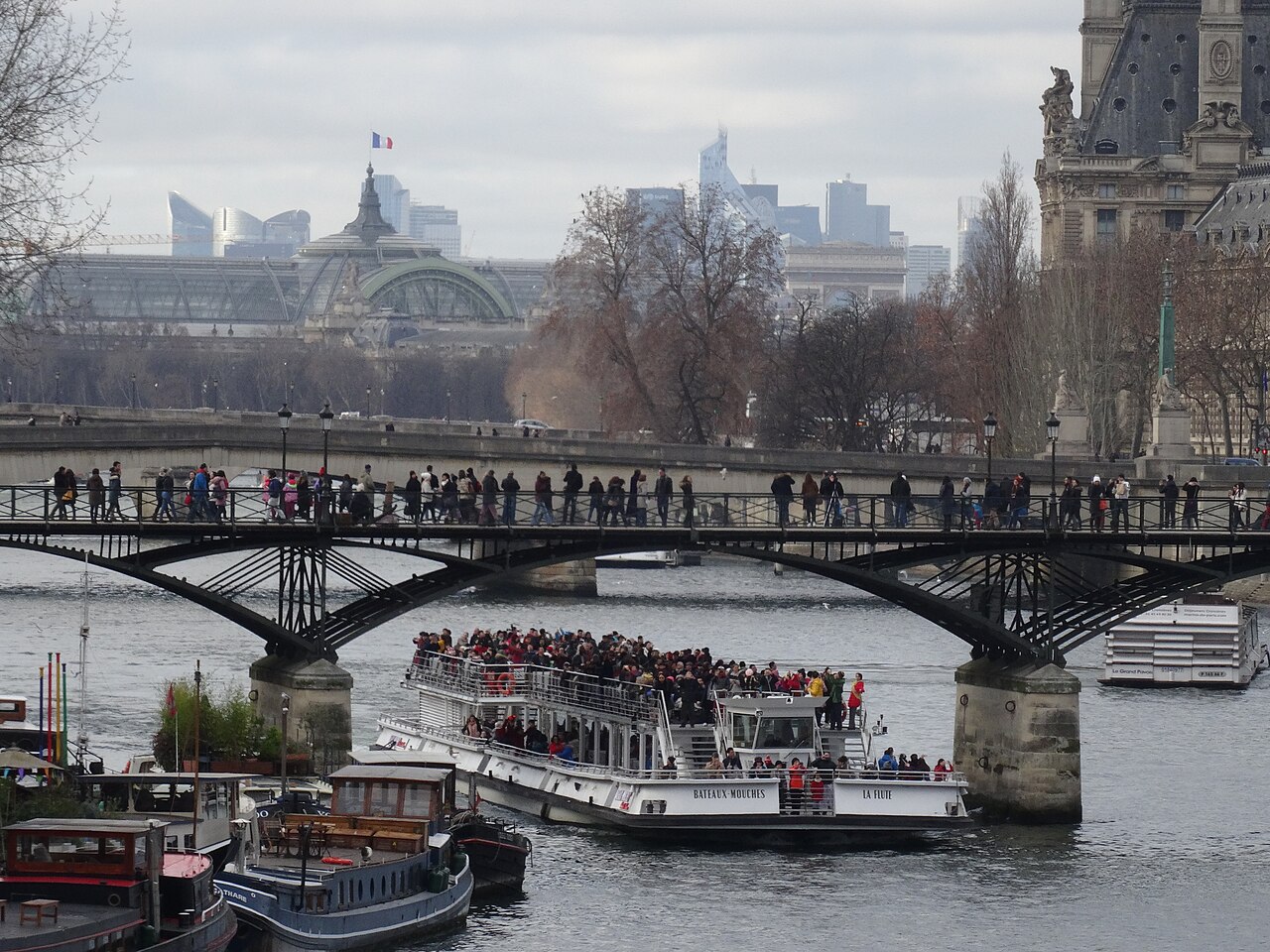 Tourists crowd a sightseeing boat and the Pont des Arts on the Seine in Paris