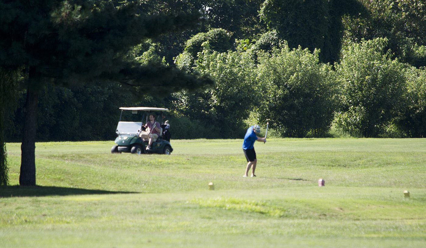 A golfer swinging a club on a tree-lined fairway at East Potomac Golf Course