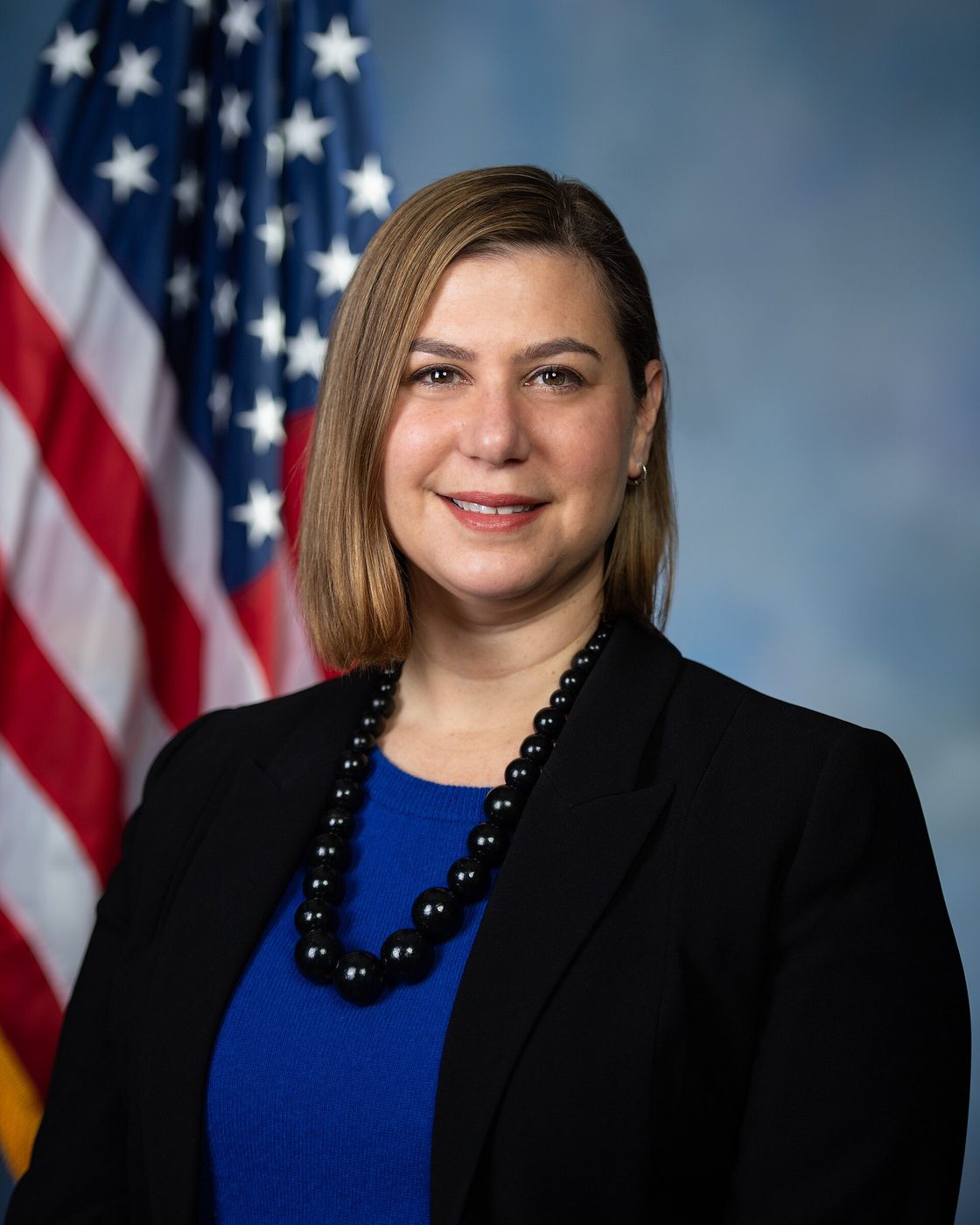 Official portrait of Elissa Slotkin in a dark jacket in front of a flag