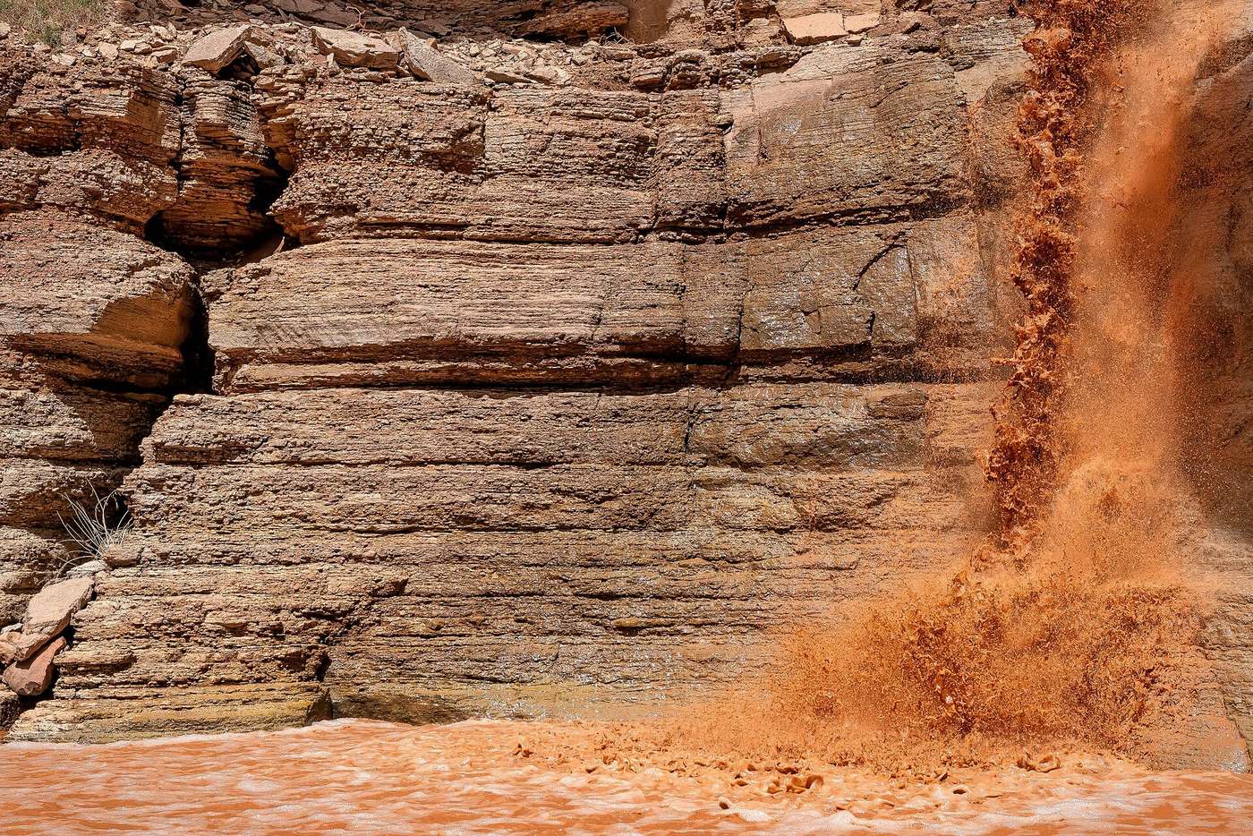 Muddy brown floodwater rushing down a desert wash in the Grand Canyon