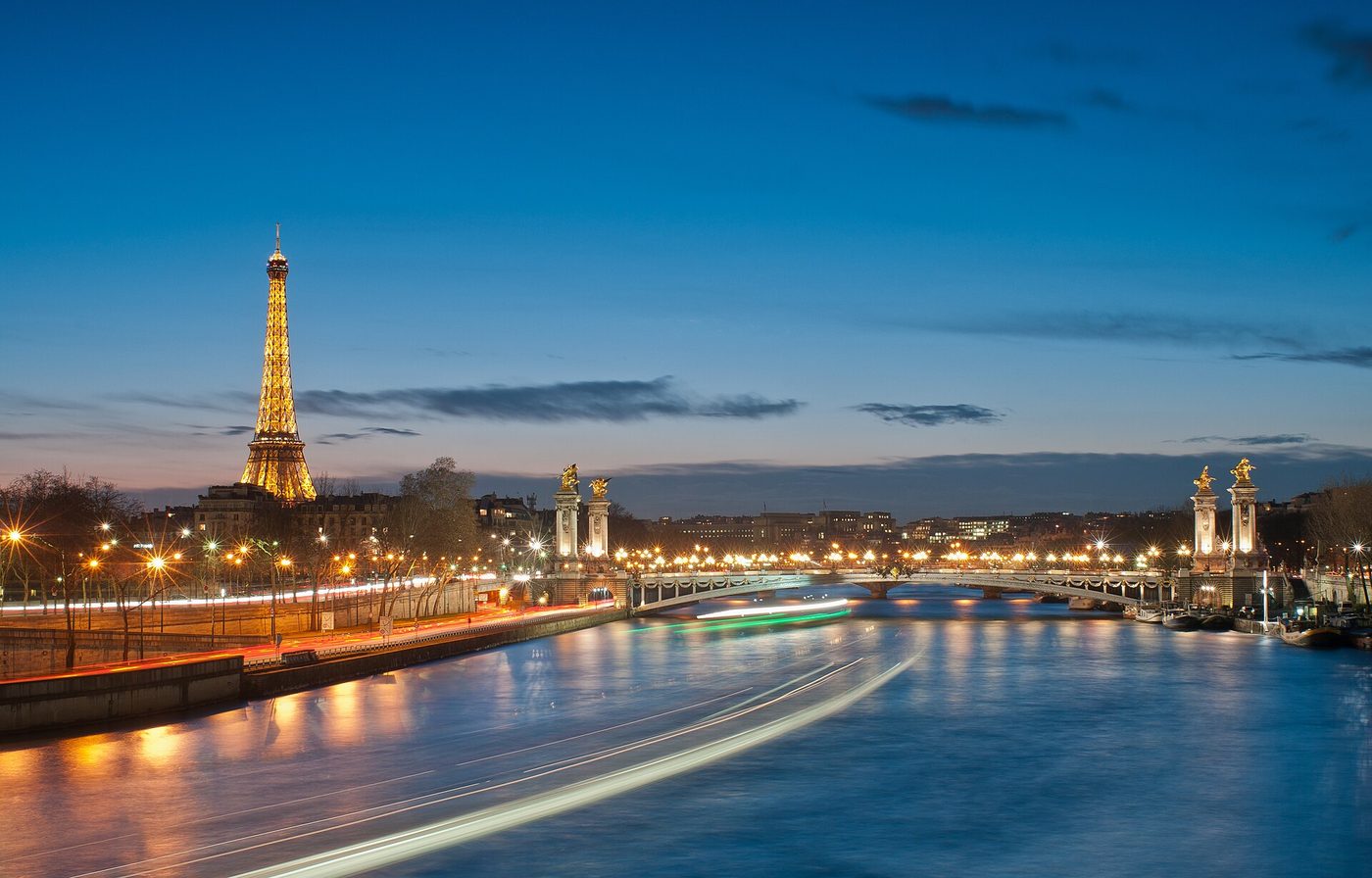 The Eiffel Tower lit up at night beside the ornate Pont Alexandre III bridge in Paris