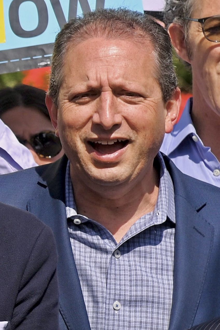Brad Lander in a blue jacket and checked shirt speaking at an outdoor rally