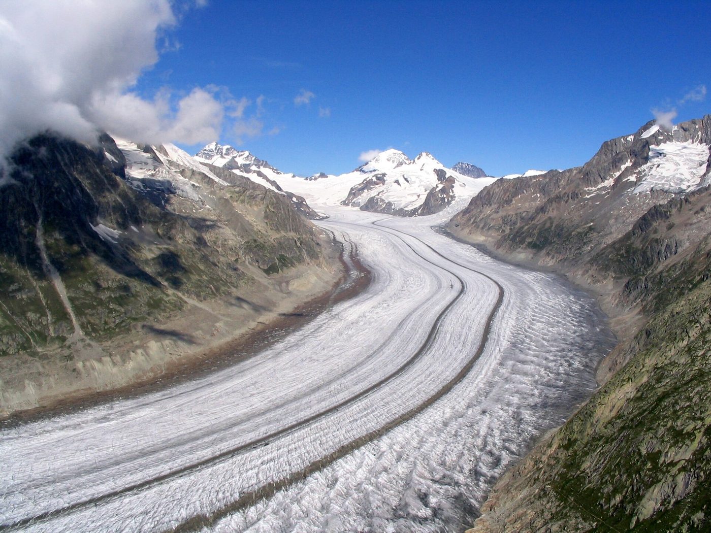 A long glacier winding down a valley between snowy mountains