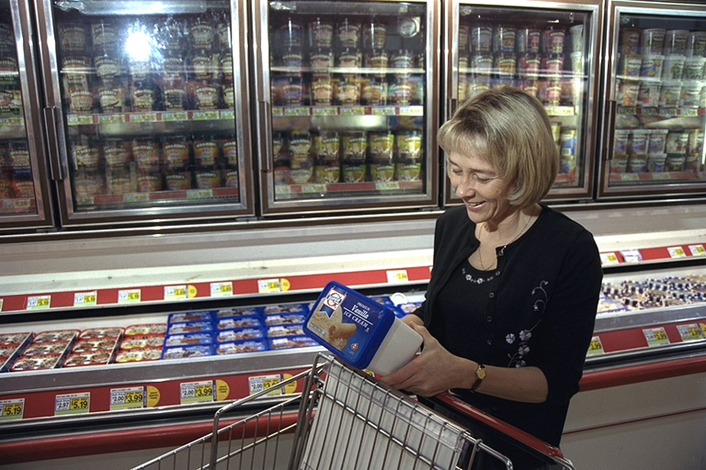 A shopper reading the label on an ice cream carton in a grocery store freezer aisle