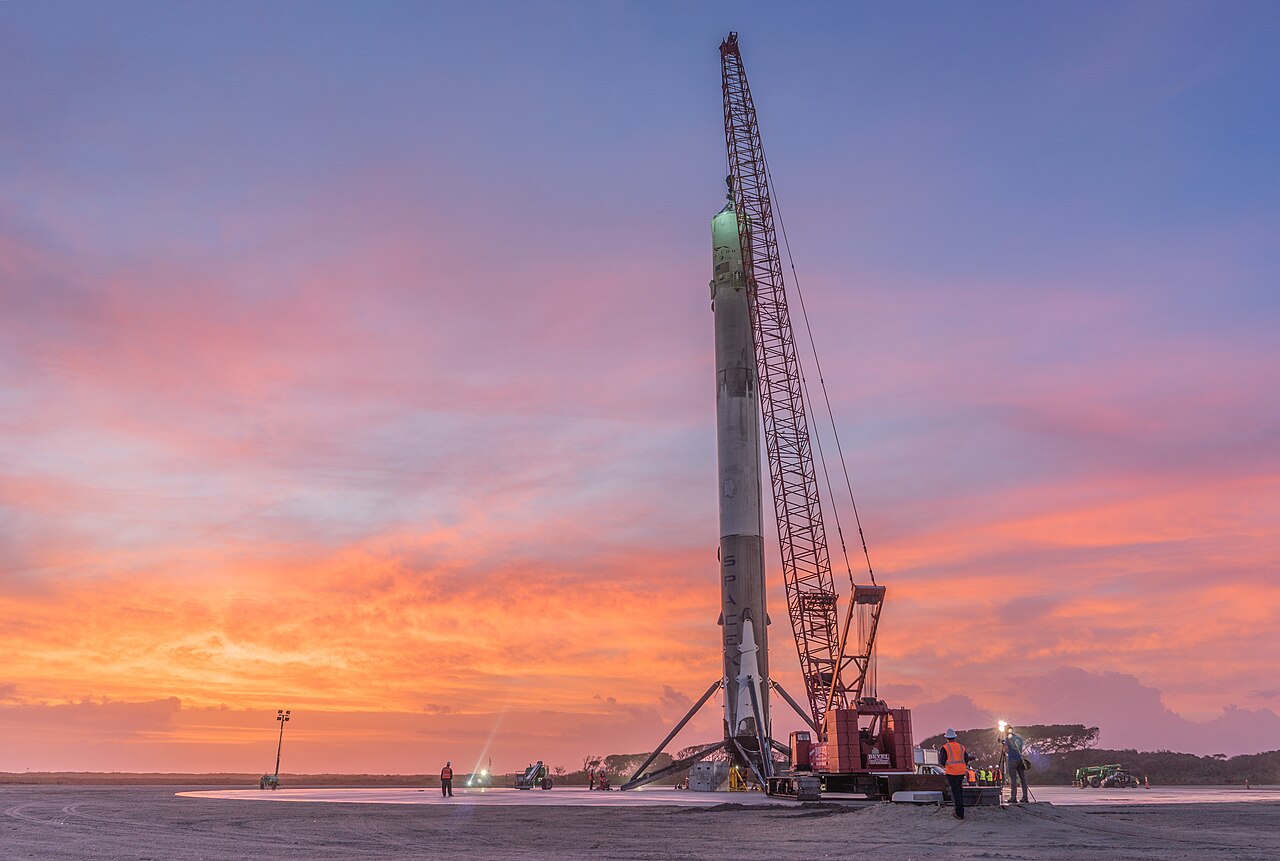 A Falcon 9 rocket booster standing upright on a landing pad at night