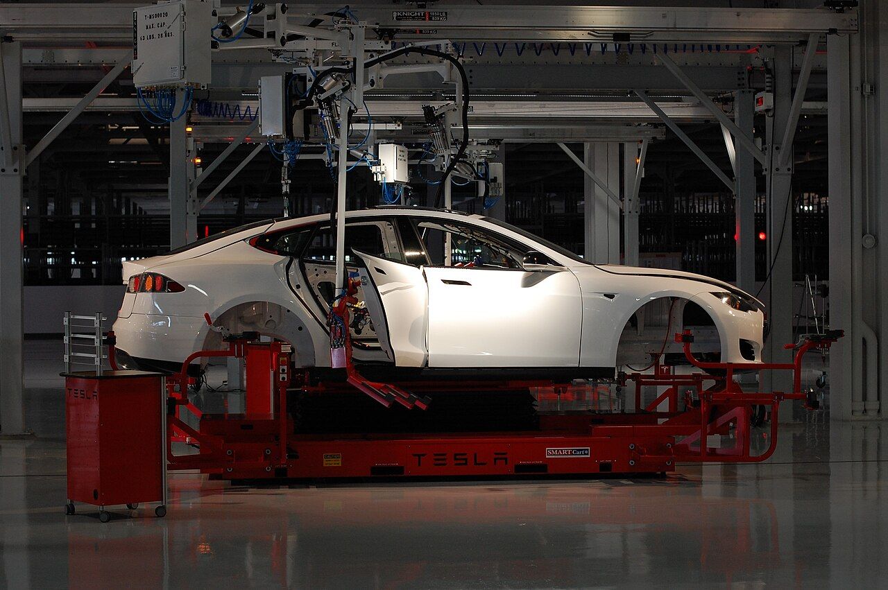 A white Tesla Model S body on a red assembly cart inside a factory
