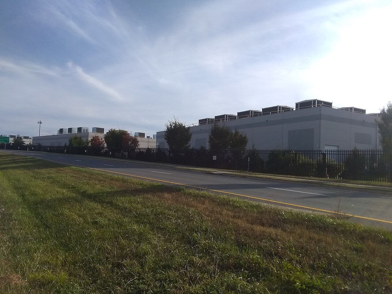 Low, gray data center buildings behind a grassy field under a blue sky