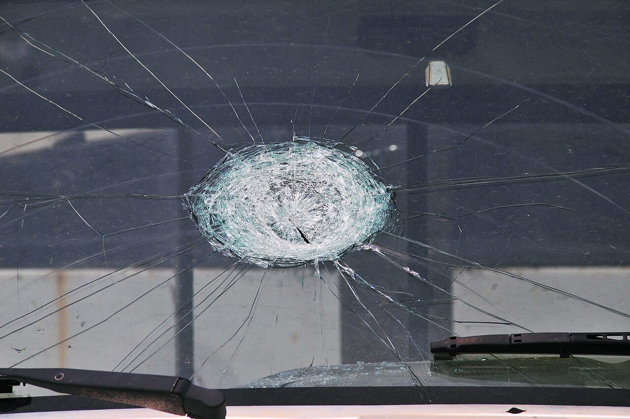 A cracked truck windshield with a round impact mark from a large hailstone