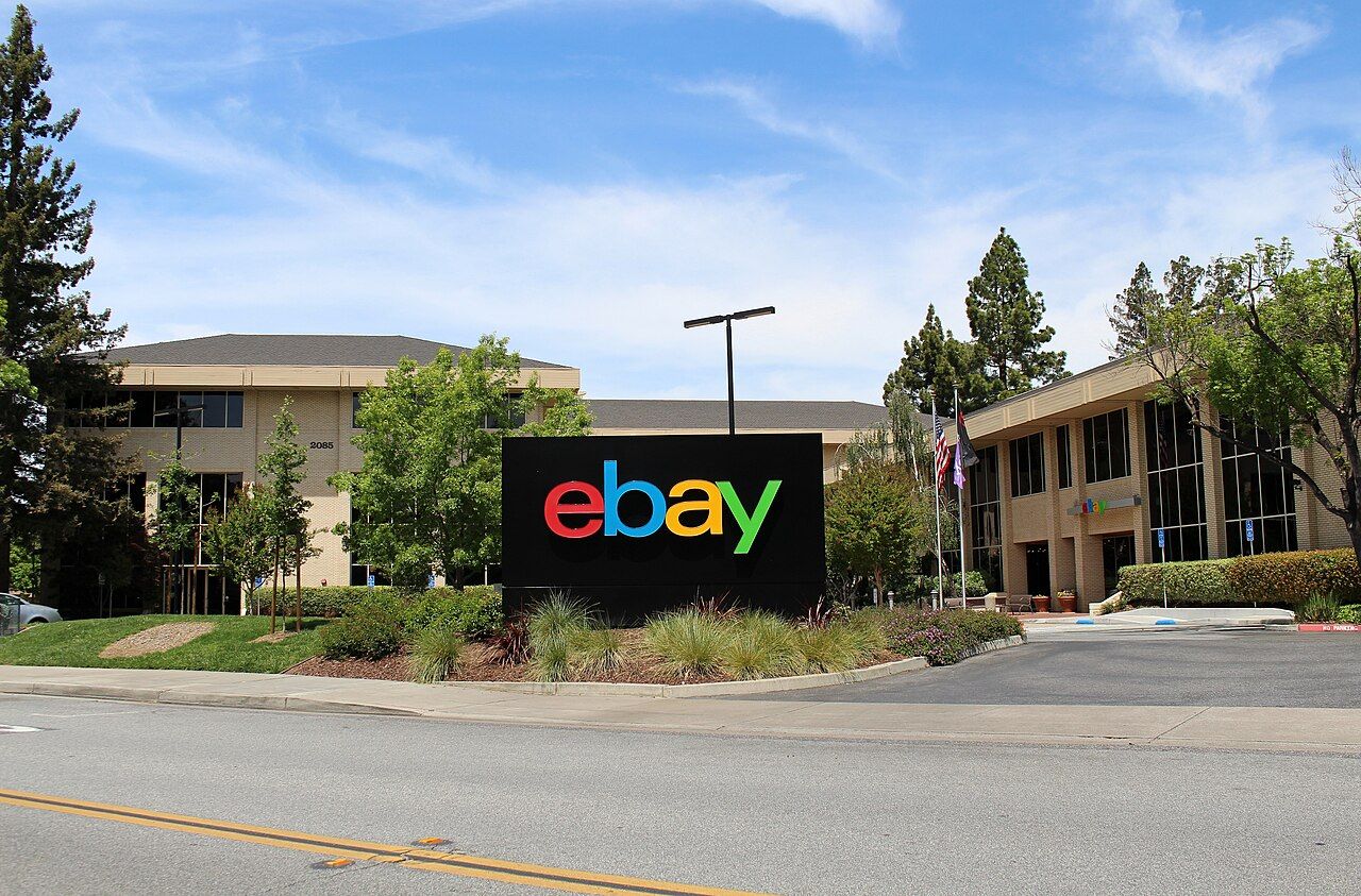 A modern office building with an eBay sign in front, surrounded by trees
