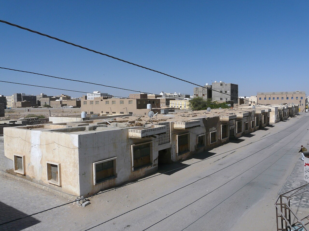 Low pale buildings along an empty street under a clear blue sky