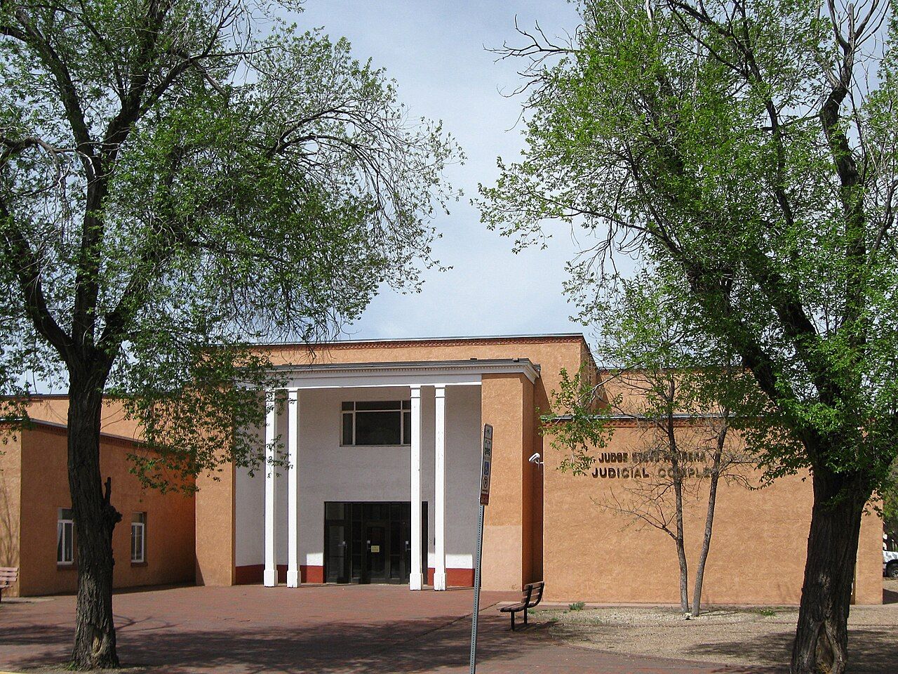 A tan brick court building with white columns at its entrance, framed by trees