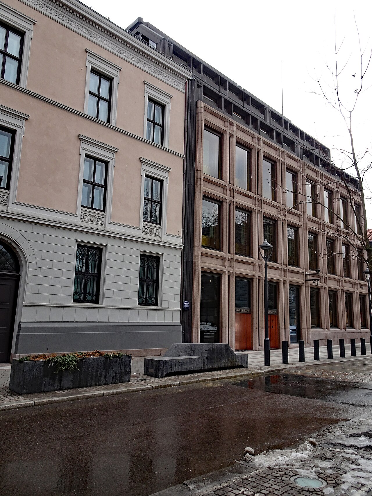 A stone building with tall windows next to a brick building on a wet street