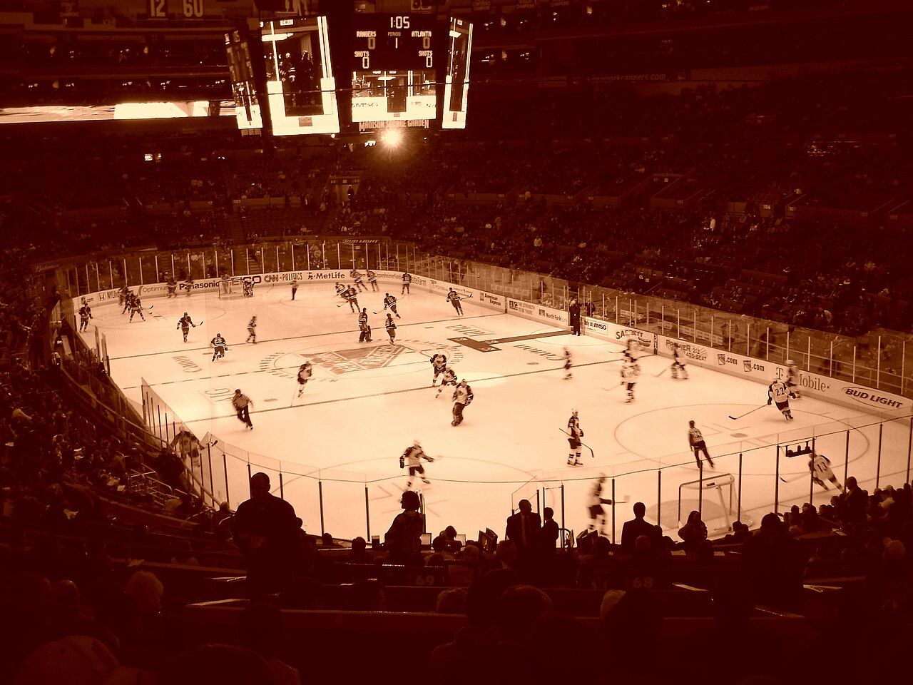 Hockey players on the ice under bright lights, seen from high in a dark arena