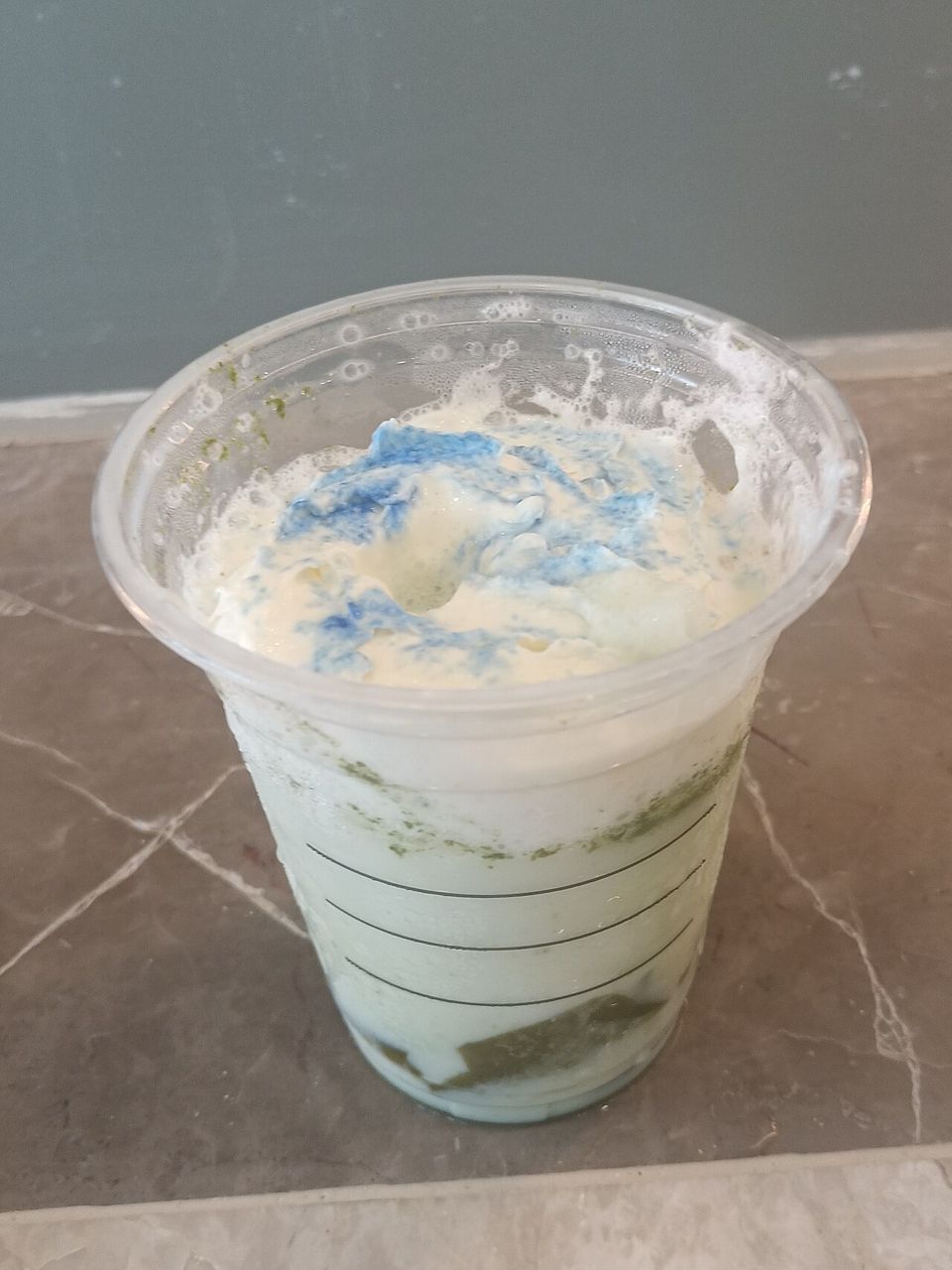 A pale green Starbucks Frappuccino with whipped cream in a clear plastic cup on a table