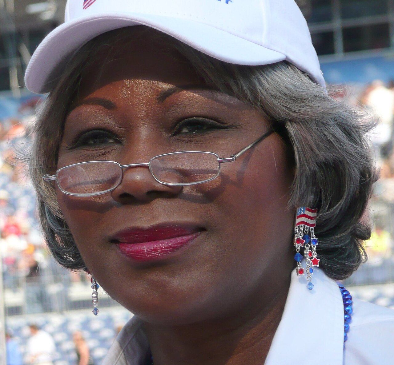Louise Lucas in a white cap and glasses smiles in a stadium