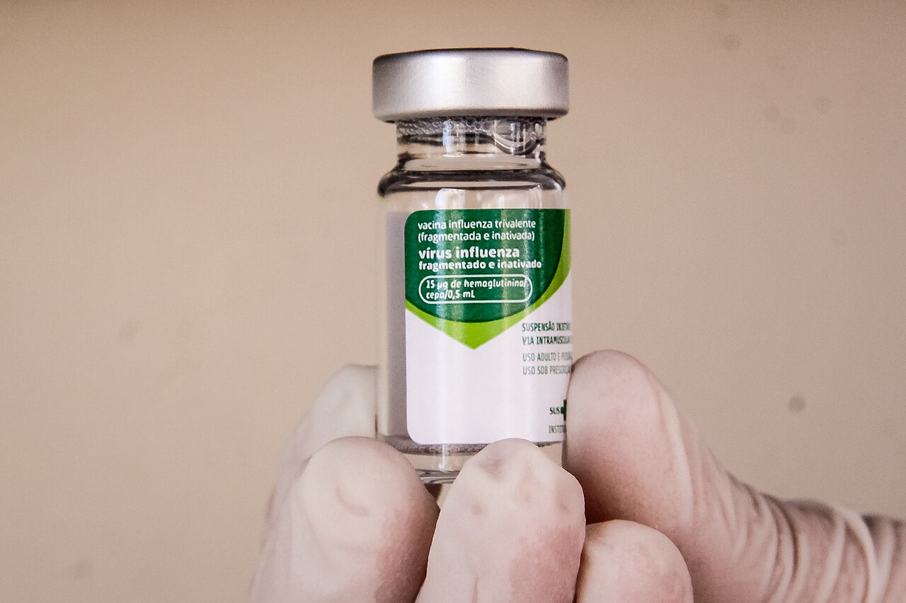 A gloved hand holds up a vial of flu vaccine