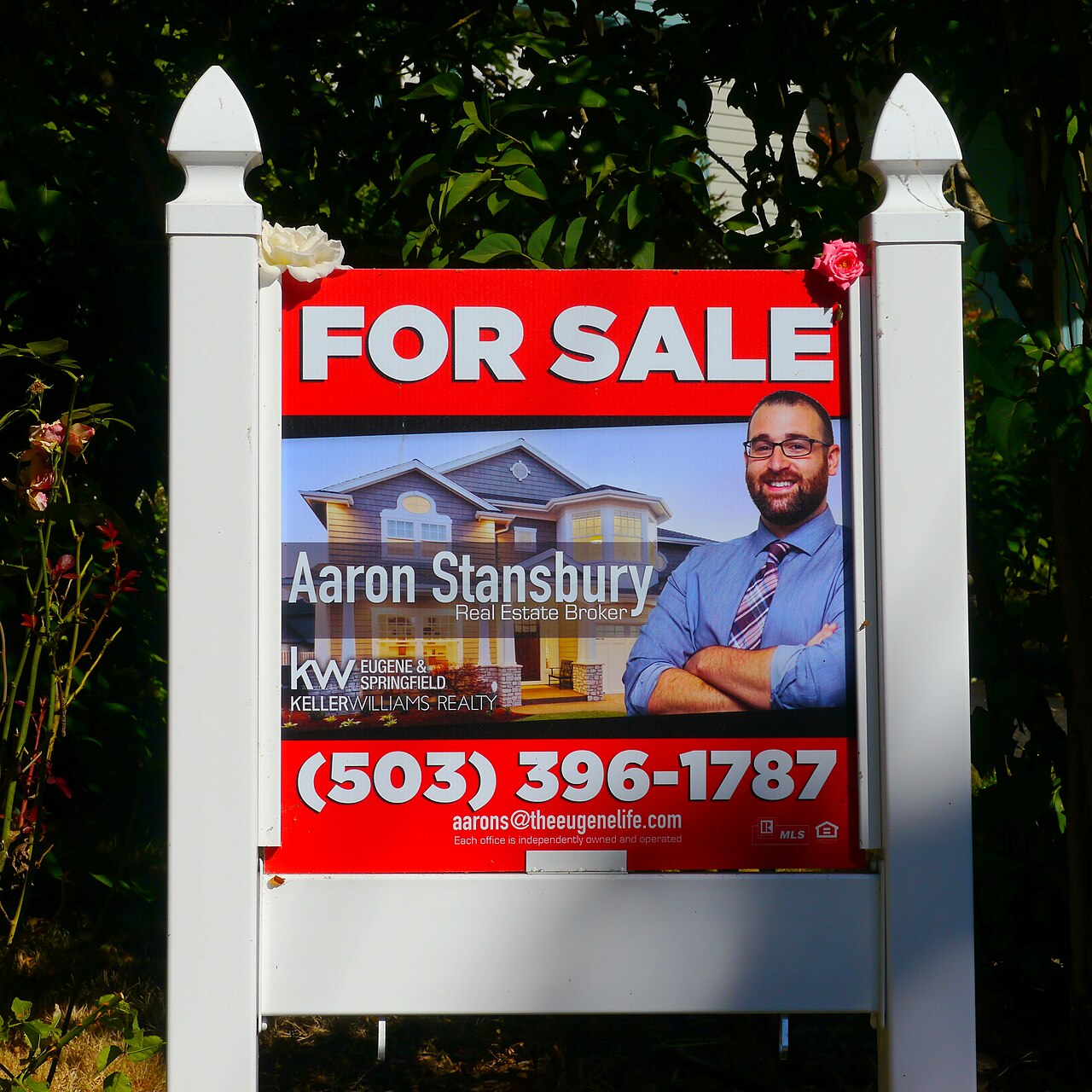 A real estate for sale sign stands on a post in front of a house