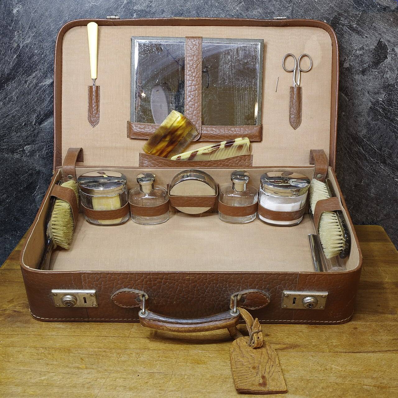 An open vintage leather suitcase holding brushes, jars and other travel accessories