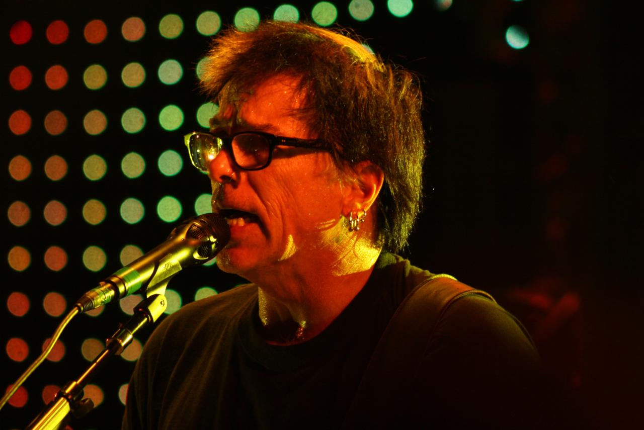 Kevin "Noodles" Wasserman playing guitar on stage under colored lights