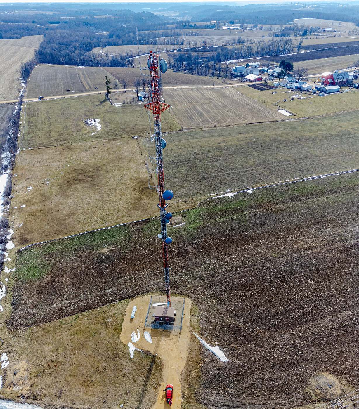 A cell tower with dish antennas among farm fields