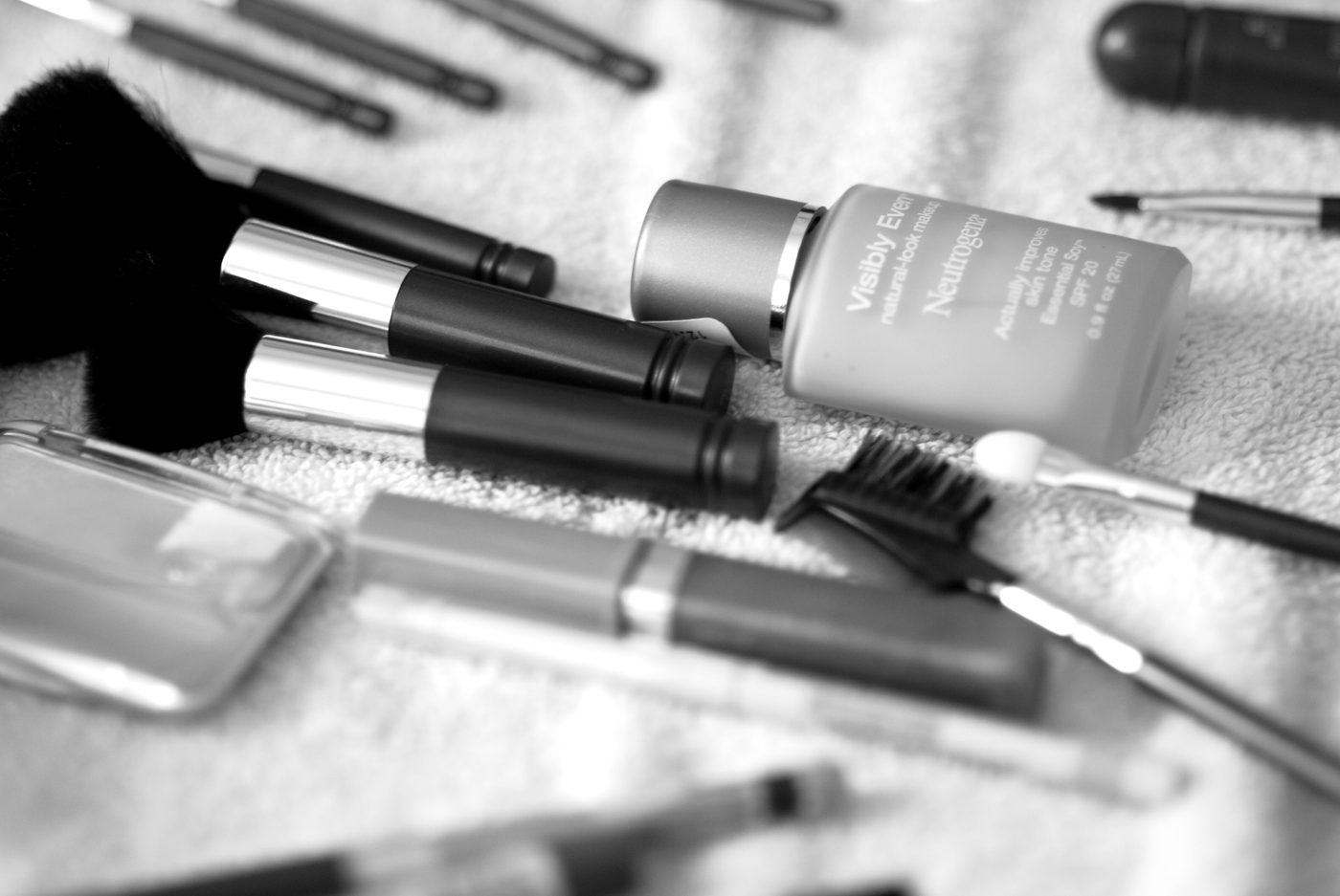 Lipsticks and makeup brushes spread across a table in black and white