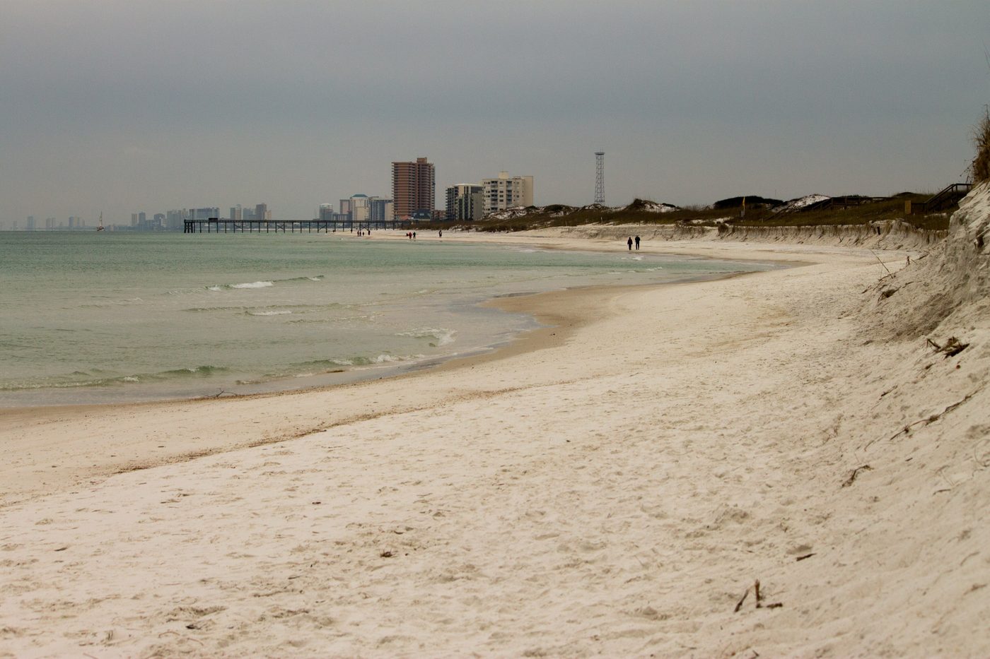 A sandy beach and calm water with hotels on the horizon