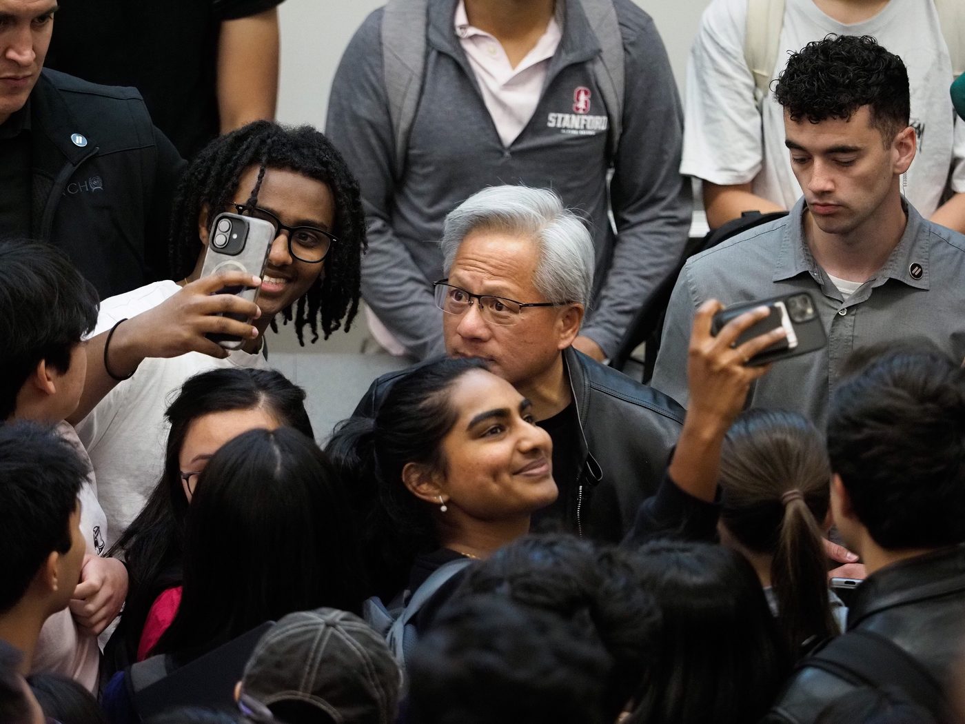 Nvidia CEO Jensen Huang surrounded by students taking selfies