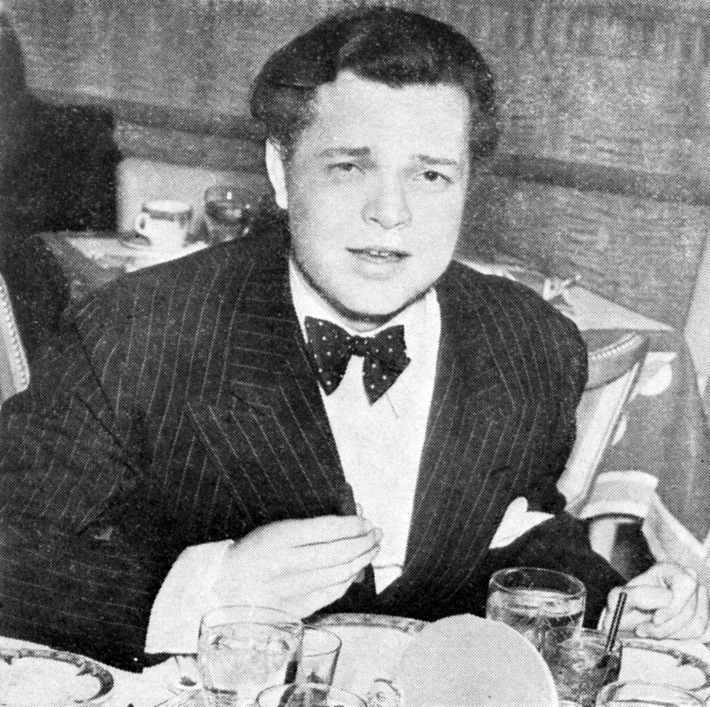 A black and white photo of a young Orson Welles in a suit seated at a table