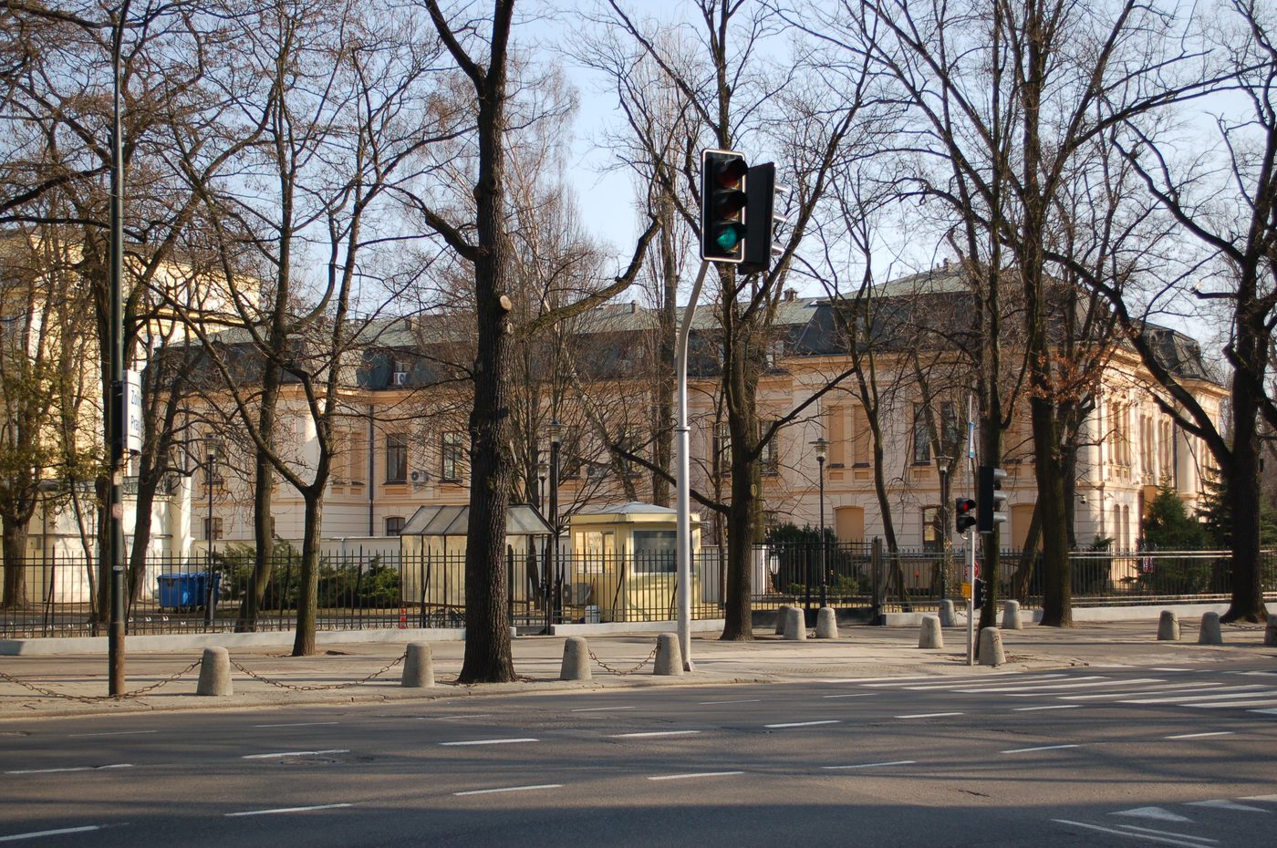 The cream-colored Constitutional Tribunal building in Warsaw seen across a street behind bare trees and a fence