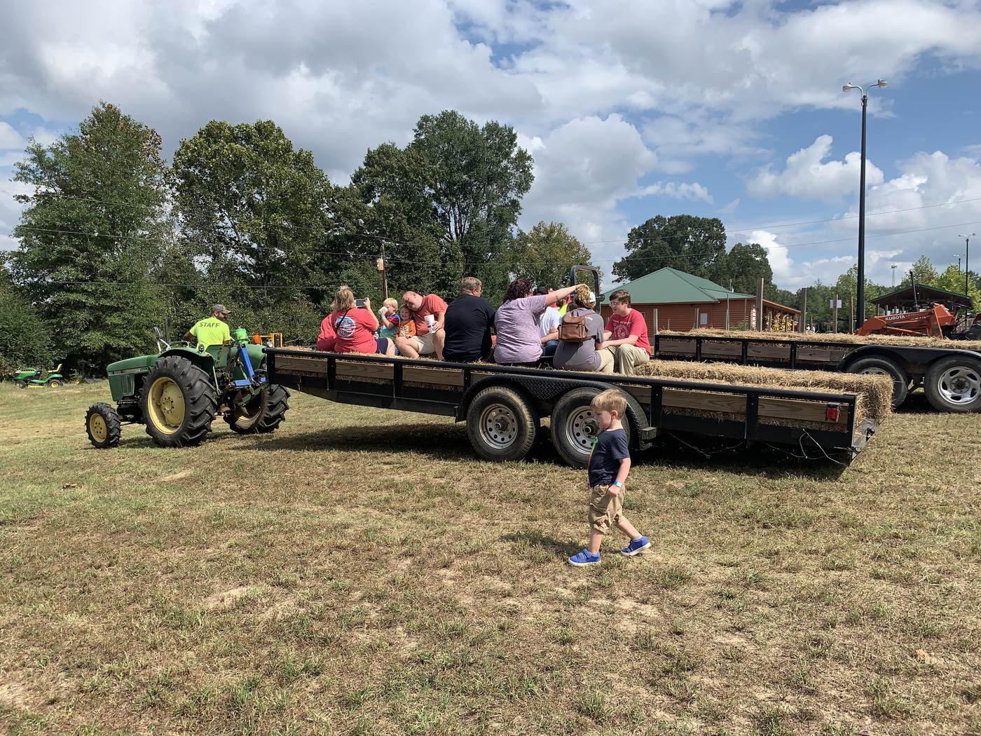 A pumpkin patch with a tractor pulling a hay wagon past rows of pumpkins