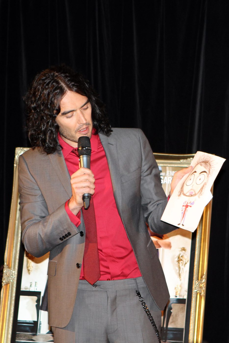 Russell Brand in a dark jacket smiling at an event