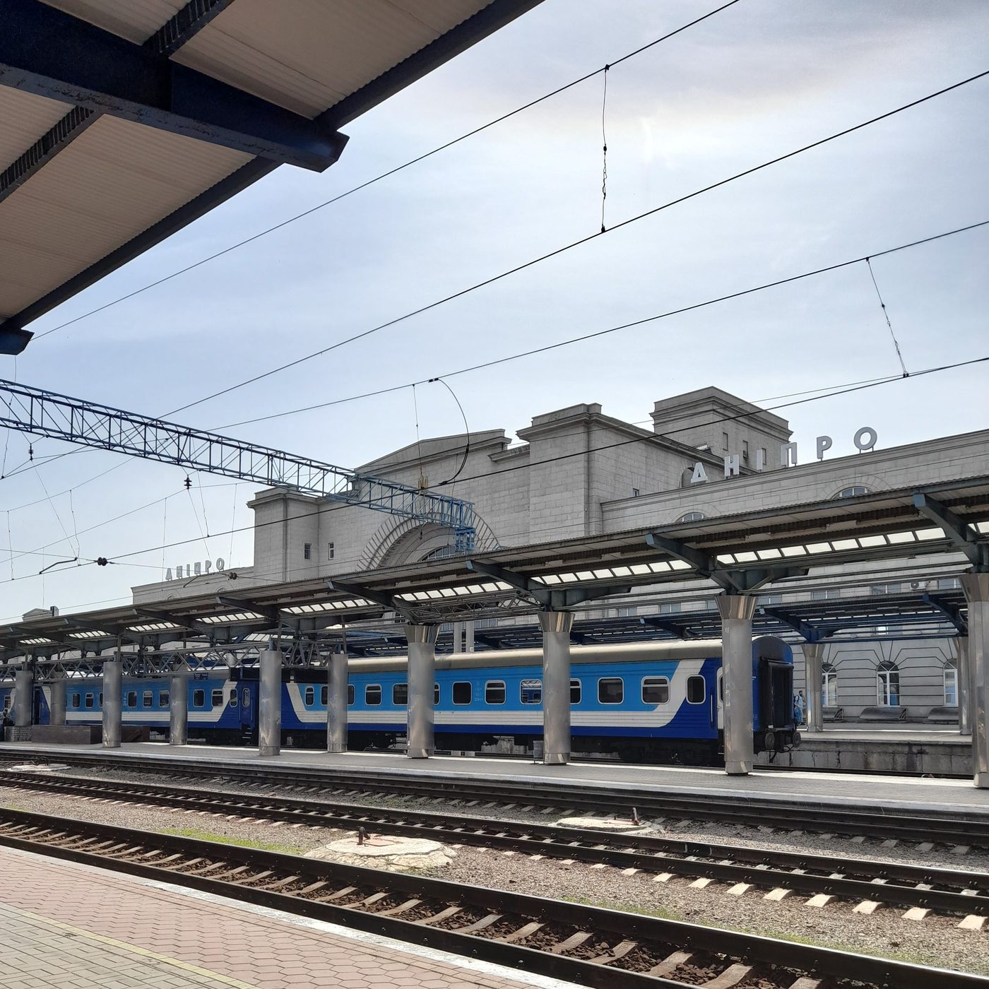 Empty platforms and tracks at the main railway station in Dnipro, Ukraine, with a blue train in the background