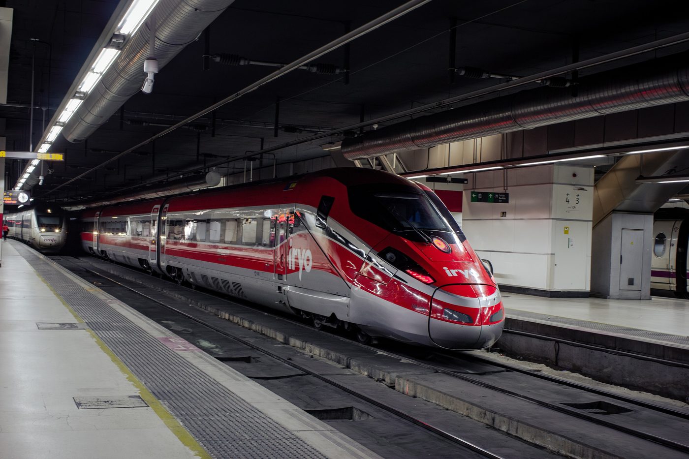 A red and white Iryo high-speed train stands at a platform inside Barcelona Sants station
