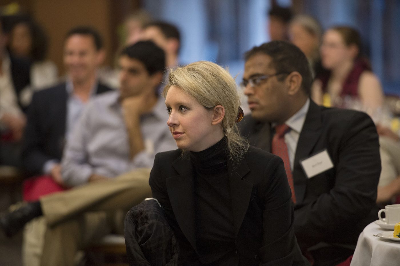Elizabeth Holmes in a black outfit listens at a Stanford panel in 2013