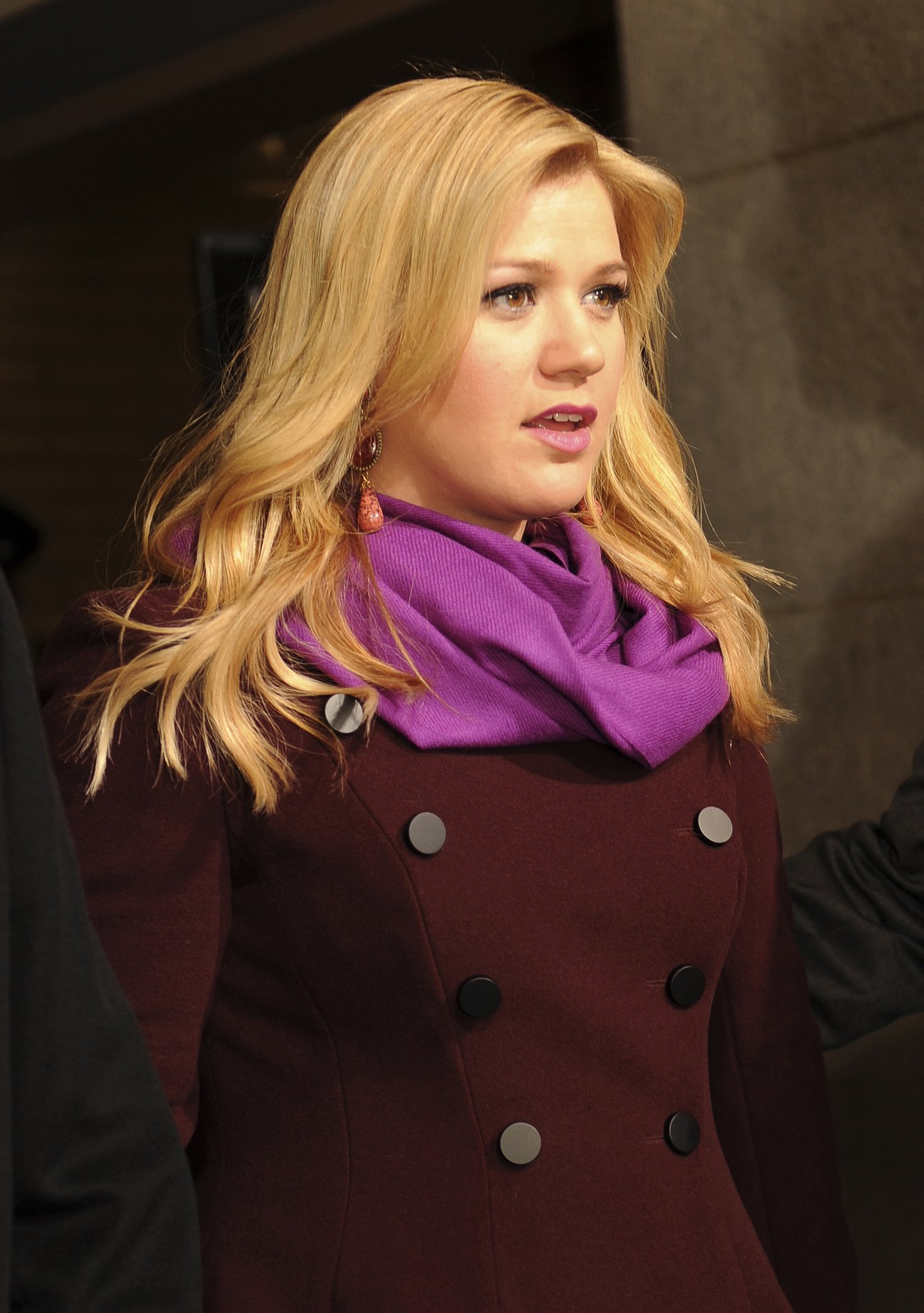 Singer Kelly Clarkson in a dark red coat and purple scarf