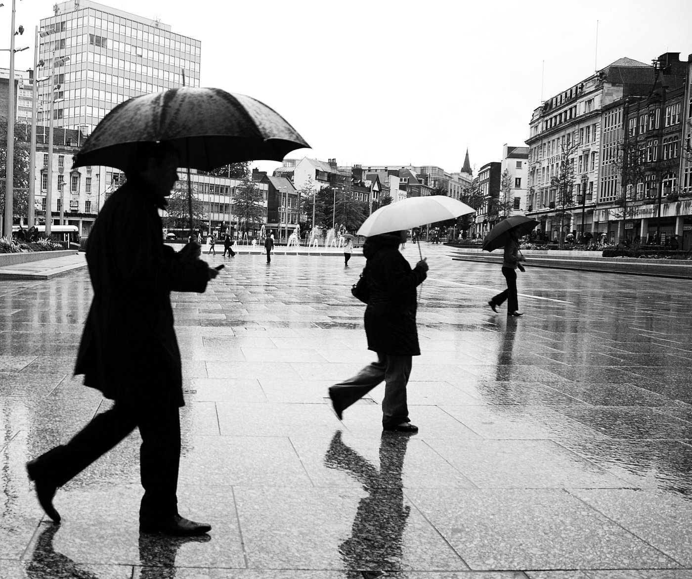 People with umbrellas walk along a wet city street in a black and white photo