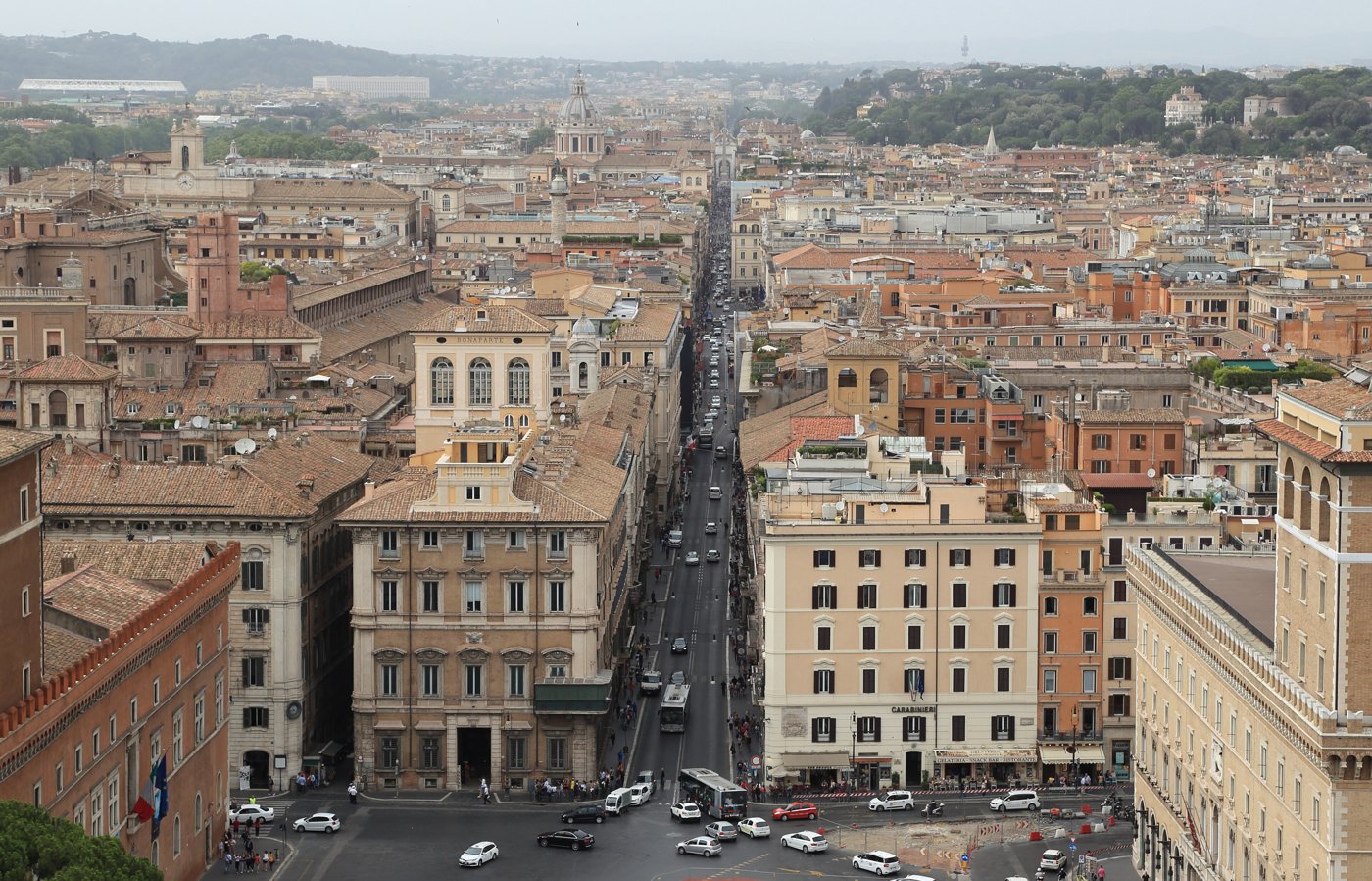A long, straight street runs between old buildings across the rooftops of Rome
