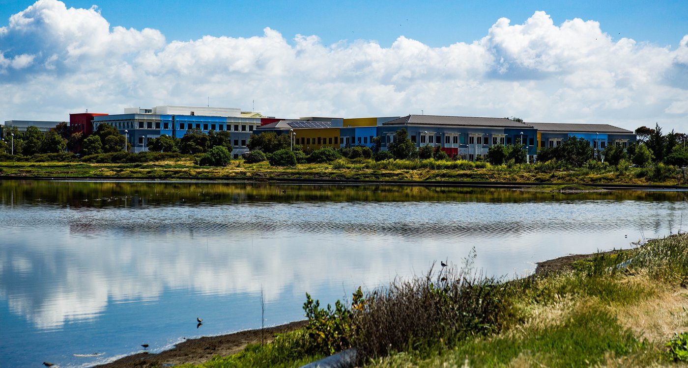 Office buildings beside a calm bay under a cloudy blue sky