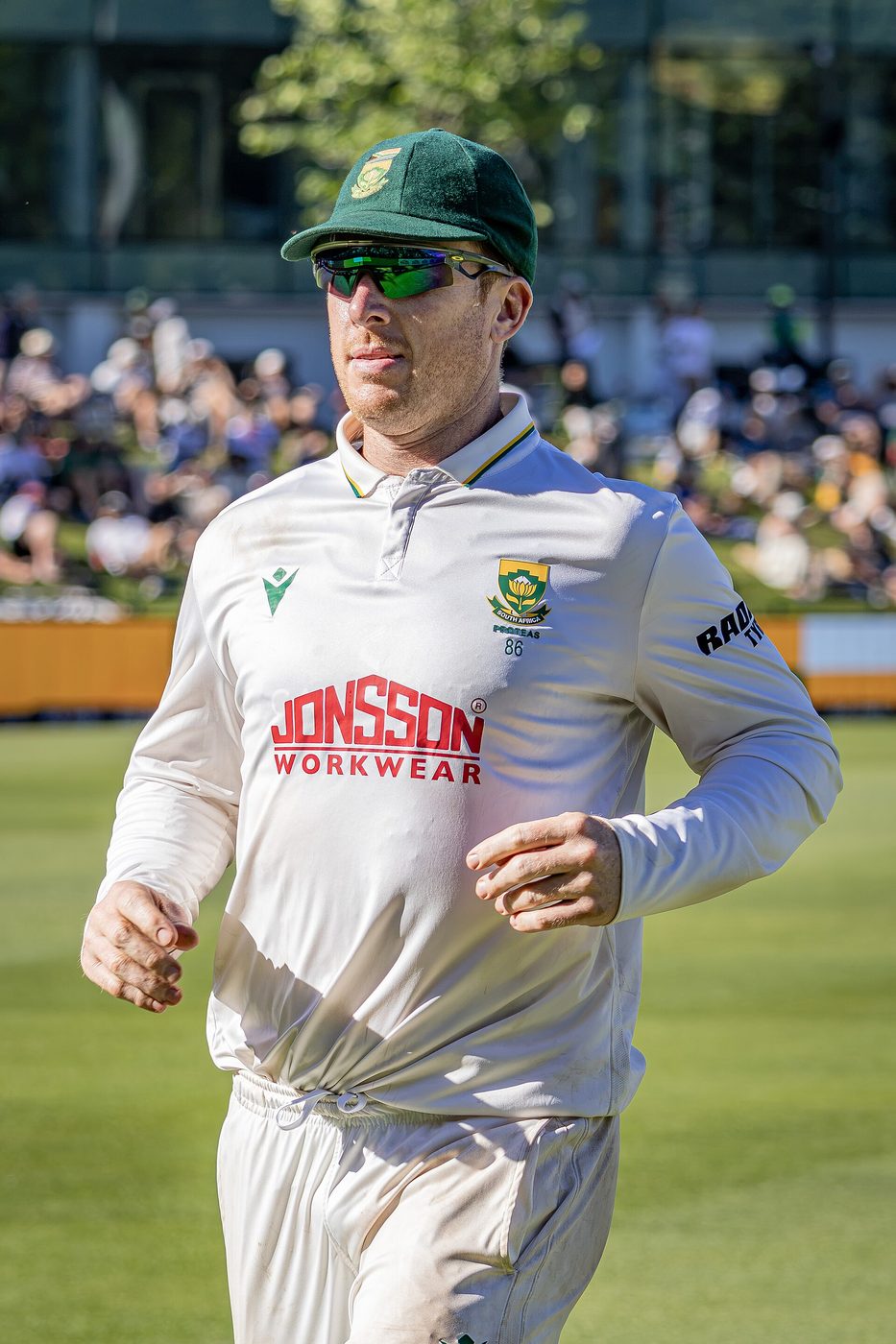 Simon Harmer jogs on the field in South Africa's white Test kit and green cap