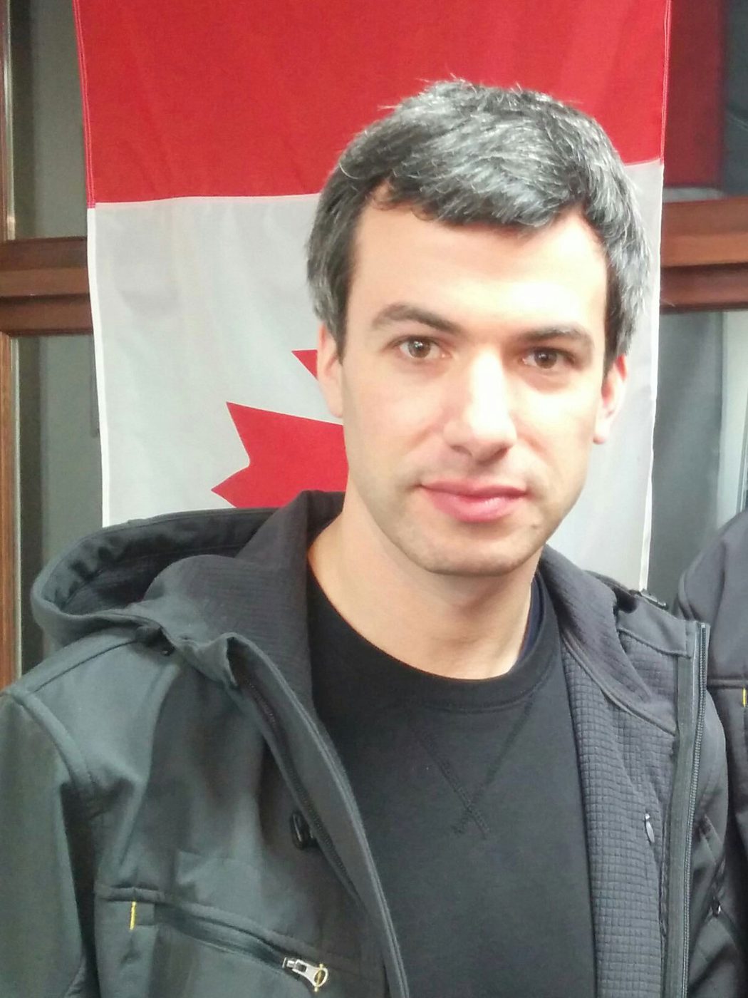 Nathan Fielder in a dark jacket in front of a Canadian flag